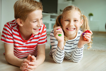 Wall Mural - Portrait of two cheerful children laying on the floor and playing with colorful dices