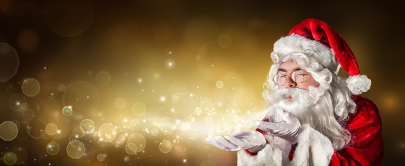 Wall Mural - santa claus blowing magic christmas lights in golden background