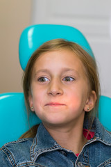 little girl sitting in a chair near a dentist after dental treatment. Little girl sitts in the dentist's office. vertical photo