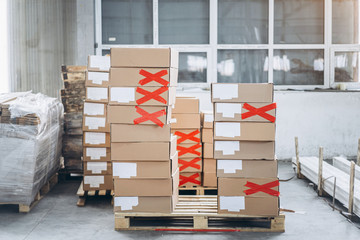 Stacks of cardboard boxes with products in the factory's packaging workshop. Some of them are marked with red tape