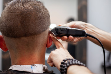 young guy makes a short haircut in a barbershop with a trimmer, close-up