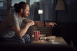 Side view portrait of contemporary man watching TV in dark and eating pop corn while enjoying late night movies, copy space