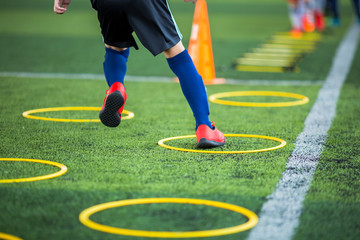 Wall Mural - Selective focus to kid soccer player Jogging and jump at ring ladder marker on green artificial turf. Equipment for training class of football academy.