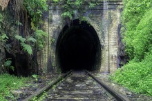 Beautiful Shot Of Train Rails Surrounded By Nature Leading To The Dark Tunnel