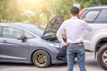 The driver is calling for insurance after a traffic accident. car crash accident on street, damaged automobiles after collision. The car crashed on a road between a saloon and a pickup.