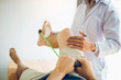 © wutzkoh - Confident physical therapist helps patient use resistance band stretching out his leg in clinic room.