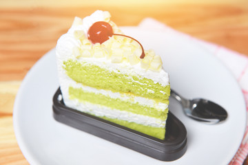 Delicious green tea cheese cake - Green cake slice with cherry fruit and cream on white palte on the table