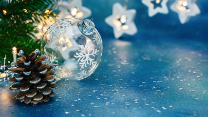 christmas tree branch decorated with glowing lights. pine cone and glass ball on blue festive background