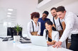 © alfa27 - young and enthusiastic people in office, stand near asian woman sitting with laptop. Discuss new project looking at screen of laptop, smiling