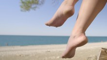 Female Legs Swing Against Backdrop Of Sea Beach. Woman Shakes Legs On Background Of Sea Beach.