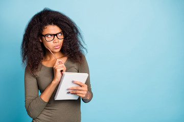 Poster - Portrait of pensive minded dark skin girl in spectacles clever smart intelligent hipster think thoughts to write essay hold copybook pen wear stylish outfit isolated over blue color background