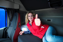 Female Truck Driver Lying On Vehicle Cabin Bed Showing Thumbs Up. Woman Professional Commercial Driver Waking Up In Her Bed Fresh And Ready To Drive. Trucker Lifestyle.