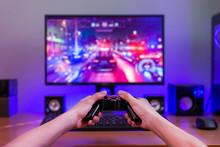Joypad In Hands. Computer Gaming Concept. Computer Display With Game In Background. RGB Light Behind The Desk.