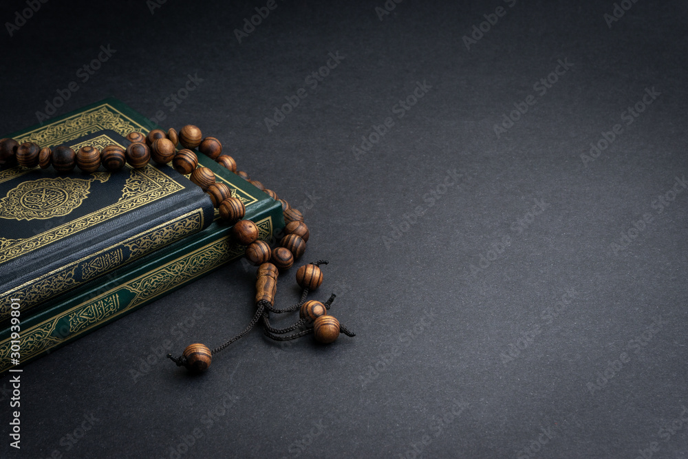 Holy Quran with arabic calligraphy meaning of Al Quran and tasbih or rosary beads on black background. Selective focus and crop fragment - obrazy, fototapety, plakaty 