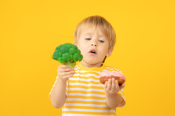 Happy child holding donut and broccoli