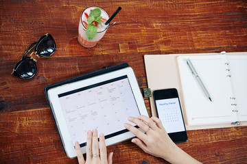 Woman checking monthly planner on smartphone and filling calendar application on tablet computer