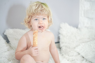 little child taking waffle and eating it with pleasure and fun on white room background