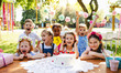 © Halfpoint - Children with cake standing around table on birthday party in garden in summer.