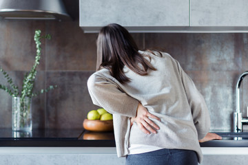 Brunette girl is holding hand on back. Young woman is feeling bad. Sudden attack of pinched nerve pain, vertebral displacement, radiculitis. Effects of hypothermia, injury, passive lifestyle.