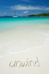 Wall Mural - 'unwind' message handwritten on smooth sand beach with incoming wave