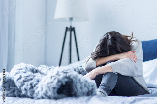 Cuadros en Lienzo Young woman in gray clothes is sitting curled up on bed at home