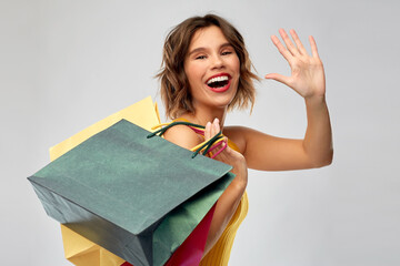 Sticker - sale and people concept - happy smiling young woman in mustard yellow top and jeans with shopping bags waving hand over grey background