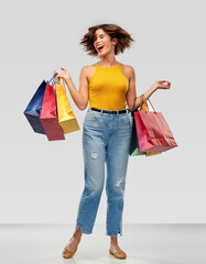 Wall Mural - sale and people concept - happy smiling young woman in mustard yellow top and jeans with shopping bags over grey background