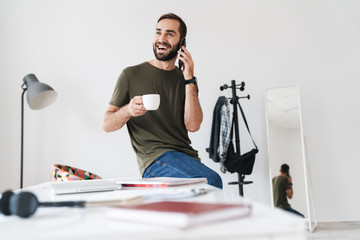 Poster - Image of caucasian laughing man talking on cellphone and drinking coffee