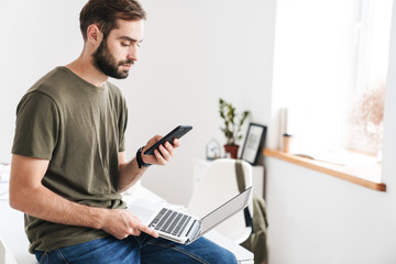 Sticker - Image of handsome serious man typing on cellphone and using laptop