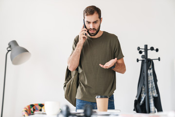 Sticker - Image of handsome perplexed man talking on cellphone while working