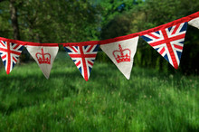 Banner Of British Union Jack Flag And Royal Crown Celebratory Bunting Hanging In Front Of A Bright Green English Summer Background