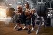 © alfa27 - Strong brutal male powerlifter doing squats using heavy barbell, young active female trainer showing the right position, preparing for serious competition of weightlifting, professional sport