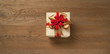 christmas gift box tied with red and golden bow over a wooden table. Horizontal composition with copy space at the left and right of the box.