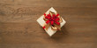 christmas gift box tied with red and golden bow over a wooden table. Horizontal composition with copy space at the left and right of the box.