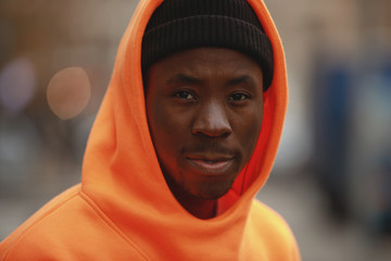 Wall Mural - Handsome African man closeup portrait wearing bright orange hoodie in city