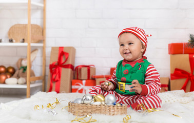 Cute baby elf playing with Xmas tree decorations at home