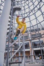 A Young Guy In A Yellow Hoodie And Turquoise Sneakers Stands On A Spiral Staircase. Teen Jumps Off With A Beautiful Spiral Staircase In The Beautiful Architecture