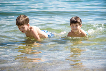 Wall Mural - Happy family playing in blue water of swimming pool on a tropical resort at the sea. Summer vacations concept. Two brother kids are best friends