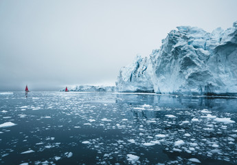 beautiful red sailboat in the arctic next to a massive iceberg showing the scale. cruising among flo