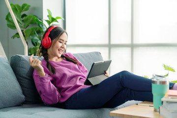 Candid of asian woman using tablet for watching online movie stream mobile device on sofa at living room. Young happy girl enjoying with entertainment media online on weekend.