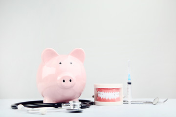 Pink piggy bank with stethoscope and teeth model on grey background