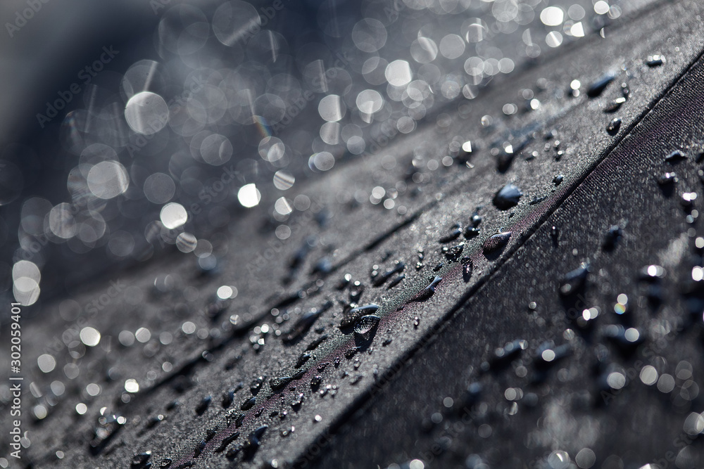 Abstract black background. Blurred raindrops with bokeh on a black umbrella. Rain Water droplets on black waterproof fabric.Raindrops in the sun. Background with free space. - obrazy, fototapety, plakaty 