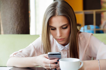 Girl reads messages on the phone while sitting in a cafe.