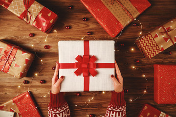 Wall Mural - red christmas gifts with hands and garlands of lights on wooden background.