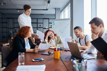 Young business people sad with result of their work, disappointed redhaired woman sit in the center of table