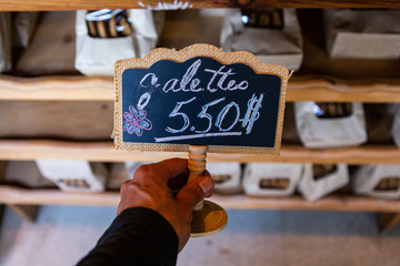 Close up of chalk hand writen backboard and wood sign at maket. Market labels for showing the price of flat cakes in french. Modern creative sings.