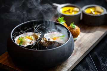 Haute cuisine - noodles with oysters filled by freezy ozone , croutons and yellow sauce on a wooden plate with dark background