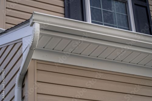Gable with vinyl siding, white frame gutter guard system, fascia, drip edge, soffit, on a pitched roof attic at a luxury American single family home neighborhood USA