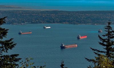 Vancouver harbor, ocean tankers waiting for loading in port white waves in a sunny day on the background scenery of blue sky and mountain range