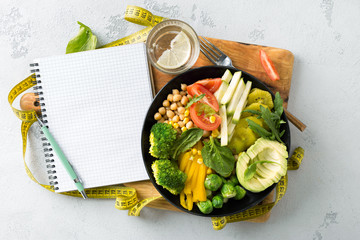 Vegan healthy balanced diet. Vegetarian buddha bowl with blank notebook and measuring tape. Сhickpeas, broccoli, pepper, tomato, spinach, arugula and avocado in plate on white background